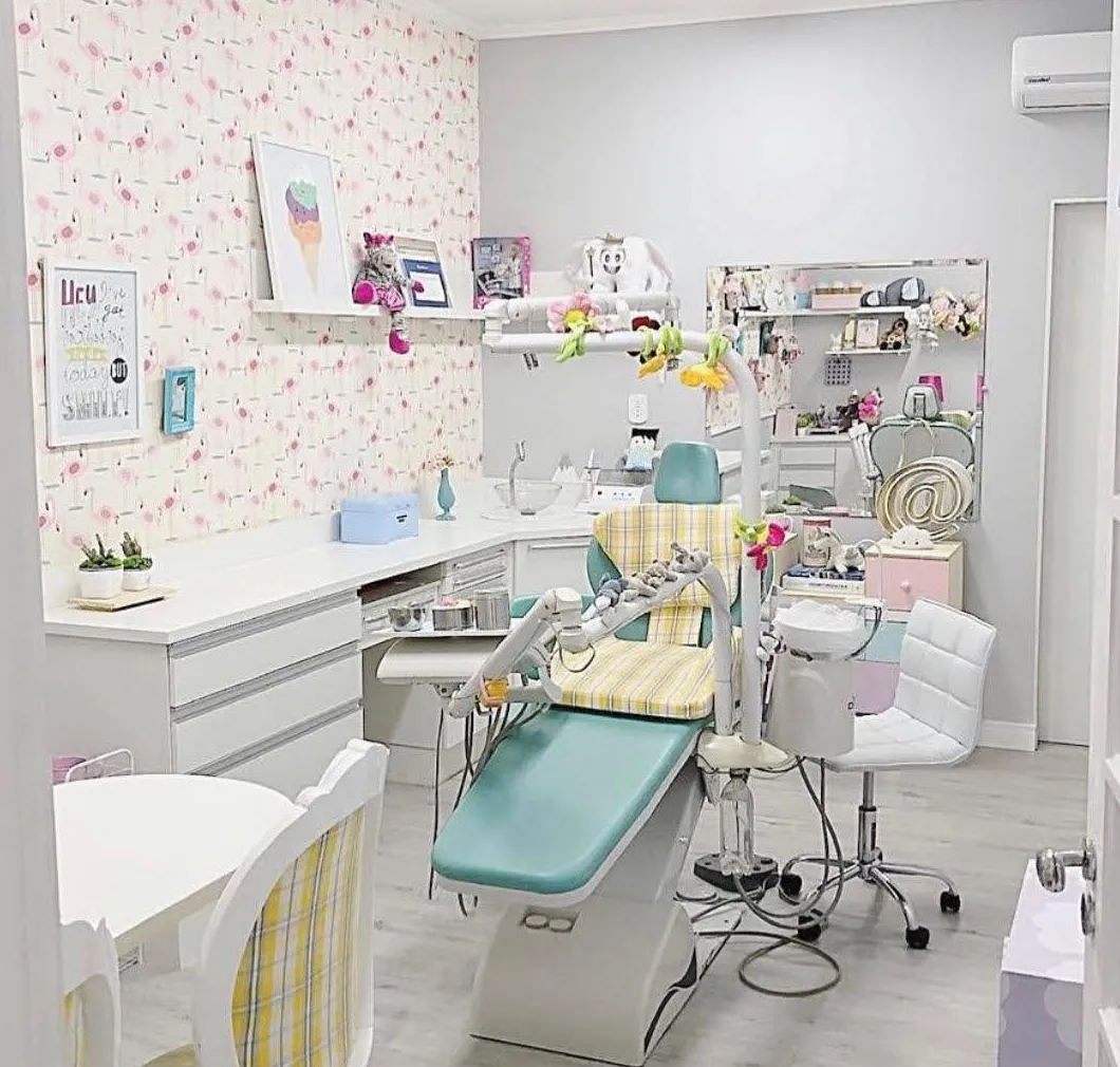 Sala de atendimento com papel de parede de flamingos, cadeira odontológica verde-água e bancada branca.